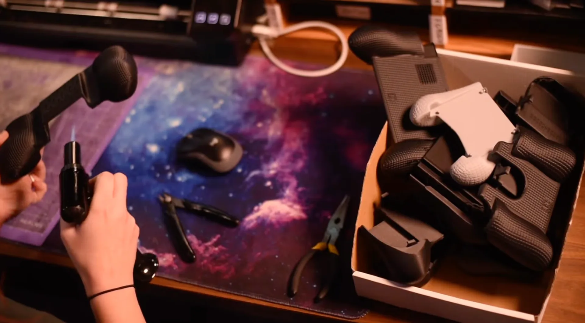 A workstation with freshly printed gaming controller grips and assembly tools laid out on a galaxy-print desk mat.