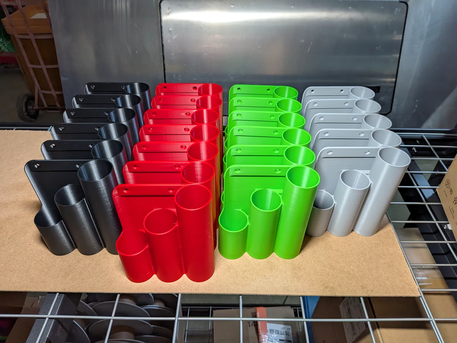 Rows of 3D-printed wall-mount tool holders in black, red, green, and gray on a wire shelf.