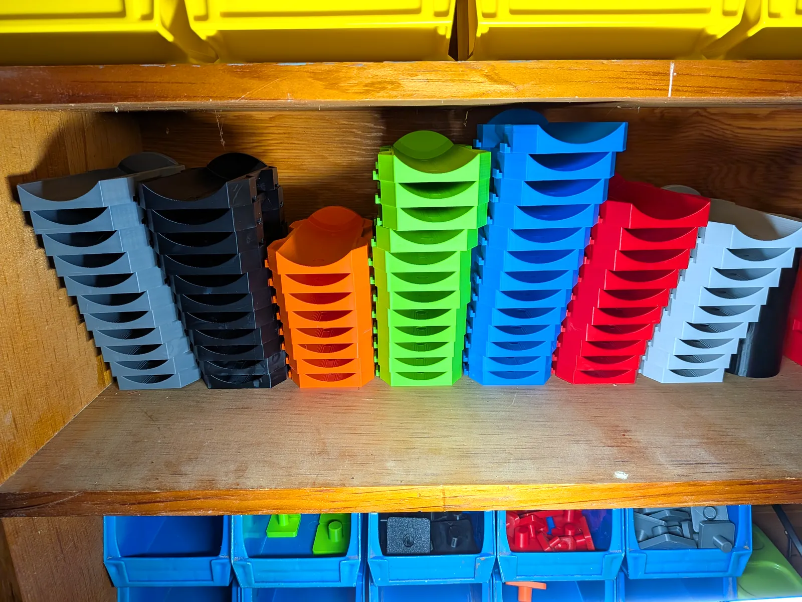 Stacks of curved 3D-printed tool organizers sorted by color: gray, black, orange, green, blue, red, and white.