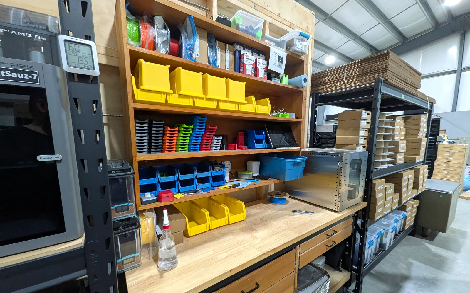 Workshop shelves stacked with finished tool-organizer products in black, orange, green, blue, red, and yellow.